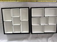 Top-down photo showing a black tray with seven white ceramic appetizer bowls of various sizes and shapes arranged inside.