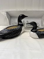 Two ceramic open back loons, one larger and one smaller, placed side by side on white surface and wall shelf in background.