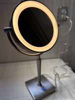 Full view of circular two-sided mirror illuminated by LED ring light on stand.