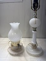 Two hobnail patterned white milk glass lamps side by side on a white surface, showing one shorter with frosting shade and one taller with no shade.