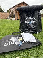 Black collapsible ice bath tub assembled outdoors with supporting legs, showing brand logo GIVFOZAY, with included accessories laid out: cover, pillow, pump, carry bag, patch kit, and drain set.