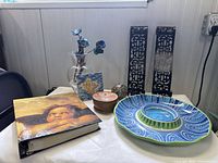 Photo showing various items: large blue and green Pier 1 ceramic chip and dip dish, small carved wooden trinket box, fish wall tile, glass ball with blue flowers, photo album, and metal wall candle sconces.