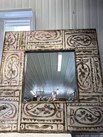 Front view of the large square mirror showing the patterned frame and central reflective surface.