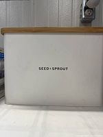 Front view of white Seed & Sprout bread box with oak lid, showing the logo on the front panel.
