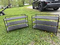 Two black metal 3-tier shoe/boot racks side by side on grass outdoors, showing their size and shape