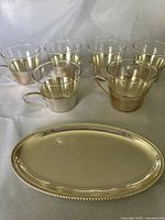 Six silver plated cups with clear glass inserts and oval silver plated sugar cube tray shown on white background.