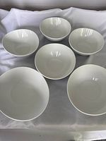 Top view showing the set of six white serving bowls arranged on a white cloth.