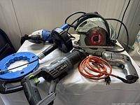 Overview of electric power tools including circular saw, angle grinder, electric drill, and one drain snake coiled on blue handle.