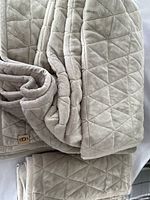 Folded beige Ugg comforter and pillow sham showing quilted diamond pattern, soft plush texture, and Ugg brand tag.