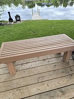 Front perspective of bench showing slatted top and leg construction on deck with lake background