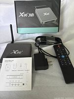 X96 Android TV box device with external antenna, power adapter, HDMI cable, remote control, and user manual in front of box packaging.