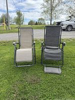 View of two zero gravity chairs side by side on grass, one beige and one black with footrest pulled out.