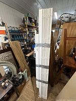 Photo of three bundled vertical window blinds secured with tape standing vertically inside a room filled with various items.