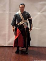 Front view of Chirrut Imwe die-cast action figure standing on a dark wooden surface with plain background showing detailed face and costume