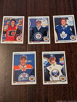Front view of five 2014-15 Upper Deck Top Draft Choice hockey cards, each featuring a different NHL player: Johnny Gaudreau, Nikolaj Ehlers, Morgan Reilly, Taylor Hall, and Jack Eichel, in their respective team uniforms on a wooden background.