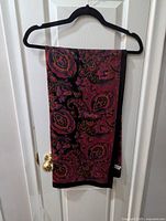 Photo showing full length of the scarf folded on a hanger, displaying the detailed floral paisley pattern in red, pink, orange, and purple on black.