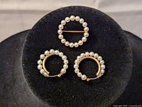 Front view of pearl pin and pair of pearl hoop earrings on black display