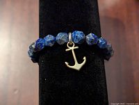 Close-up view of the blue faceted bead bracelet showing the silver-colored metal anchor charm on a black display stand