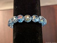 Close-up photo showing the multi-faceted clear blue glass beads strung together on the bracelet displayed on a black background.
