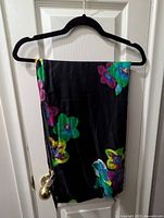Scarf folded on a black hanger showing vibrant floral patterns on a black background.