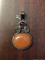 Front view of women's silver pendant showing large goldstone and smaller amethyst in silver with swirl accents.