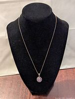 Front view of necklace on display bust showing delicate silver chain and oval purple pendant with cubic zirconia halo.