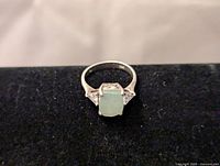 Front view of the sterling silver ring featuring a rectangular green gemstone and two small clear side stones on black velvet background