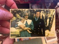 Postcard showing Diana holding a baby with Prince Charles standing beside her outdoors