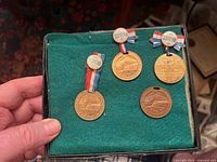 Four brass anniversary souvenir coins displayed on green felt, three with ribbon and 'Souvenir' pins, one without ribbon or pin.