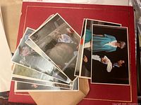 Stack of British royal family postcards resting on a red folder, showing front photographic images with glossy finish and white borders.