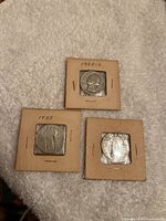 Three US silver quarters in cardboard holders marked with dates 1925 and 1935 showing significant wear.