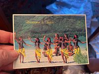Photo showing a postcard titled 'Bienvenue à Tahiti' with dancers in yellow skirts on a beach scene.
