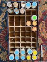 Overhead view of a cardboard grid box holding various clear plastic tubes and paper-wrapped rolls filled with uncirculated US Mint coins.