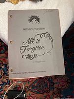 Cover of 1985 Paramount 'All is Forgiven' network television script showing gray cover with Paramount logo and script title, three-ring punched with some handwriting on top right corner.
