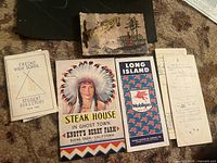 Photo showing all items in the lot including the Knotts Berry Farm menu with a Native American chief cover, the Fresno High School directory, the Socony Mobilgas Long Island map, and the aged documents including a folded paper and a small photo book.