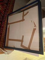 Front view of the large black wood picture frame showing glass and beige matting inside.