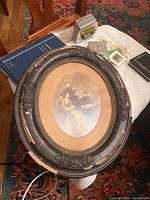 Oval black wooden frame with floral decorations showing paint chipping and wear. Sepia tone print of Abraham Lincoln with his family inside the frame. Background shows furniture and carpet.