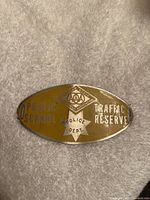 Oval yellow-golden metal traffic reserve plaque with embossed lettering from California State AAA Association, Public Schools Police Dept, about 4x2 inches.