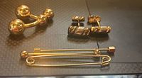 Two pairs of gold-tone cufflinks and three gold-tone tie bars arranged on a black surface