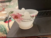 Miniature white milk glass coal hopper decorated with pink flowers and stencil text reading 'Souvenir of Manchester, NH' on front side.