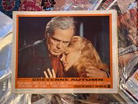 Lobby card for Cheyenne Autumn showing close-up of two characters embracing, with orange border and film credits