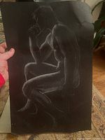 Seated nude male figure sketch in white chalk or pastel on black paper.