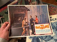 Color lobby card showing a man and woman outside a cabin and two men in suits in a forest setting from the film "The Happening".