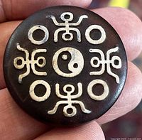 Top side of the round flat dizzy bead showing the yin yang symbol in the center and four surrounding circular and symmetrical shapes.