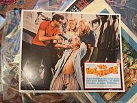 Lobby card for The Happening featuring actors in a dramatic scene with firearms, clear vibrant color photography under Columbia Pictures.