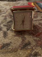 Front view of the Westclox traveling alarm clock with brass tone and white dial, in red case.