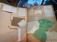 Two facing scrapbook pages showing brittle, torn paper, various glued-in scraps including fabric sample and a green tissue piece, multiple handwritten notes and typed clippings.