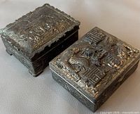 Front and angled top view showing two antique metal boxes with raised dragon and figure relief designs