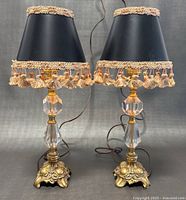 Pair of vintage glass and brass table lamps with black fabric shades trimmed with beige and peach tassels, showing full view front angle.