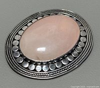 Front view of oval pink quartz brooch set in silver with decorative border